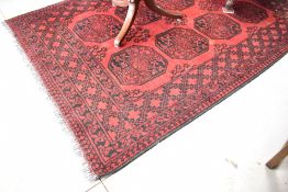 A vintage Afghan rug, having deep red ground with contrasting black geometric pattern and border,