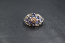 A 14ct gold diamond and possibly tanzanite set ring, the floral motif ring set with diamond chips