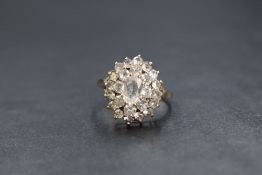 A 9ct gold white sapphire set cluster ring, the central oval cut sapphire in a step layer