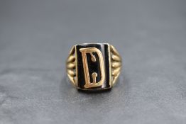 A gent's yellow metal signet ring stamped 9ct having a curved black panel bearing a yellow metal