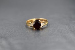 A yellow metal garnet & cubic zirconia ring having a central oval garnet flanked by two small
