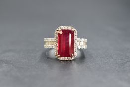 An 18ct white gold ruby and diamond set cluster ring, the central emerald cut ruby measuring approx