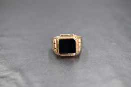 A 9ct gold onyx set signet ring, the central square onyx panel having a decorative border and