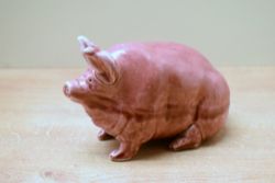 A Wemyss ware pottery pink glaze pig study, signed to base, damaged to ear, measures 11cm tall.