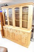 A modern pine bookcase comprising glazed section over four drawers and two double cupboards, width