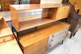A vintage teak high sideboard, possibly Nathan, having glazed shelves and drop down cocktail section