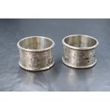 A cased pair of late Victorian silver napkin rings, having foliate scroll engraving, bead thread and