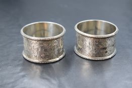 A cased pair of late Victorian silver napkin rings, having foliate scroll engraving, bead thread and