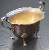 A George V silver sugar bowl, having a Chippendale style rim with scroll handles, raised on four