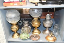 A quantity of brass and metal oil lamps and glass chimneys, some marked but not all, (1 shelf),