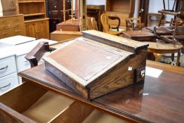 An early 20th Century oak lap desk having leather inset to slope top and fitted stationery