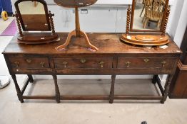 A period oak dresser base having three drawers with brass escutcheons and drop handles on turned