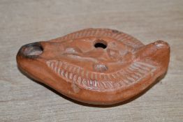A small late Roman-style red ware pottery oil lamp, of elongated form having a faint central figural