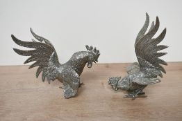 Two mid to late 20th-century white metal fighting roosters, featuring expressive plummage in a