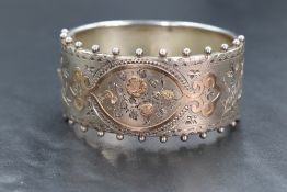 A Victorian silver hinged bracelet, having a beaded border to the engraved and gilt floral side,