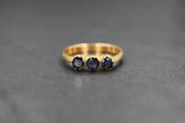 A yellow metal sapphire trilogy ring having three mid blue old cut sapphires in claw set mounts on a
