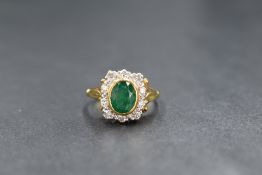 An 18ct gold emerald and diamond rectangular cluster ring, the central oval bezel set emerald approx