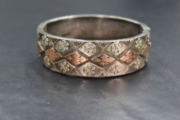 A Victorian silver hinged bangle having rose gold coloured panels & floral applique decoration