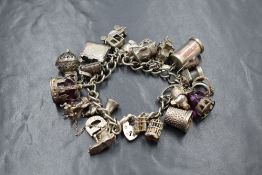 A silver curb link bracelet, having a heart padlock clasp and approximately twenty-eight charms,