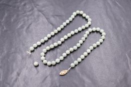 An 18' knotted string of jadeite beads of even form with a yellow metal clasp stamped 14K