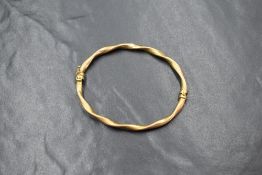 A yellow metal presumed gold hinged bangle, of a twisted design, unmarked, 3.7g