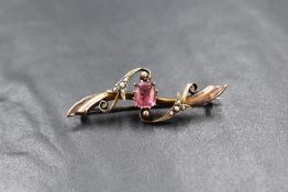 A 9ct rose gold bar brooch having a pink paste central stone with seed pearl set swirl decoration,