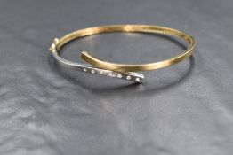 A 9ct gold diamond set hinged bracelet, having a cross over design with seven diamonds set to the