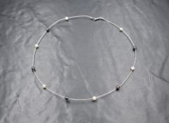 An 18ct white gold pearl set necklace, the gold wire having eleven black and white pearls, marked