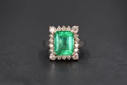 An 18ct white gold emerald and diamond cluster ring, the central emerald cut emerald measuring