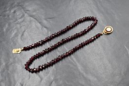 A string of facet cut garnet beads, on red thread with a pictorial set yellow metal presumed gold