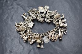 A silver curb link charm bracelet, having approximately thirty-five charms including an opening