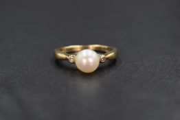 A 9ct gold cultured pearl ring having a central pearl flanked by two diamond chips on a 9ct gold
