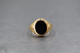 A 9ct gold onyx set signet ring, the oval onyx panel having rubbed decoration to the shoulders,