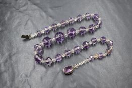 A string of graduated facet cut amethyst beads having small clear plastic spacer beads, on clear