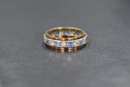 A yellow metal presumed gold topaz set full eternity band, having alternating princess cut blue