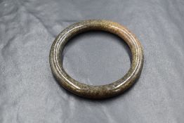 A carved jade bangle, having dark grey-brown tones with fibrous texture visible 5.5cm internal