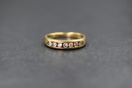 A yellow metal eternity ring, presumed gold having seven channel set cubic zirconia, size K & 2.6g