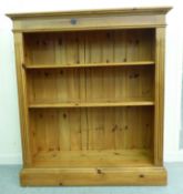 A modern honey coloured pine open front bookcase with two height adjustable shelves, on a plinth