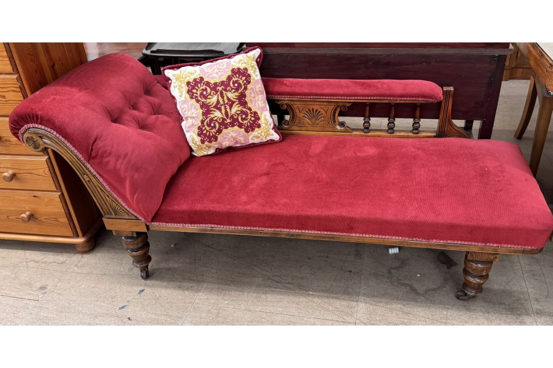 A Victorian chaise longue upholstered in red with a spindle back on turned legs and casters