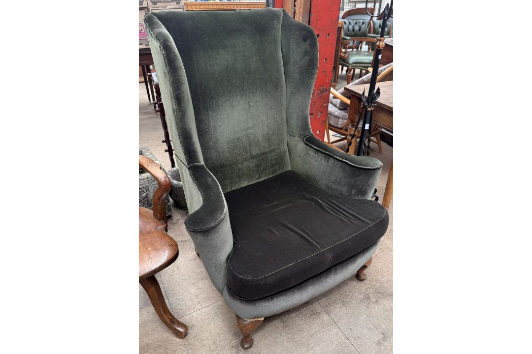 An upholstered wing back arm chair with outswept arms on cabriole legs and pad feet