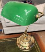 A desk lamp with a green glass shade and brass column