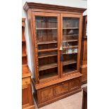 A large pine bookcase with a moulded cornice above a pair of glazed doors,
