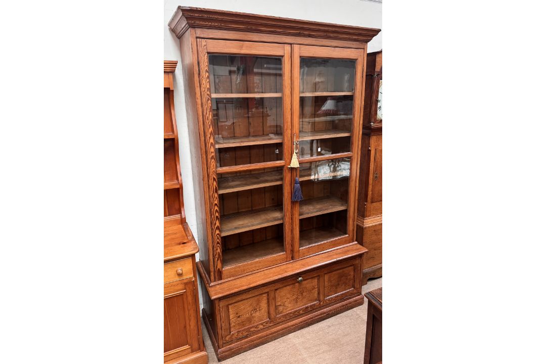 A large pine bookcase with a moulded cornice above a pair of glazed doors,