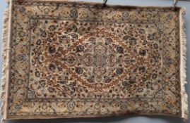 A cream ground Kashan rug with a central blue medallion, multiple flower heads and leaves,