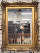 A gilt wall mirror of rectangular form decorated with scrolling leaves and flowers with a bevelled