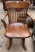 An elbow chair with a slat back and solid seat on four splayed legs