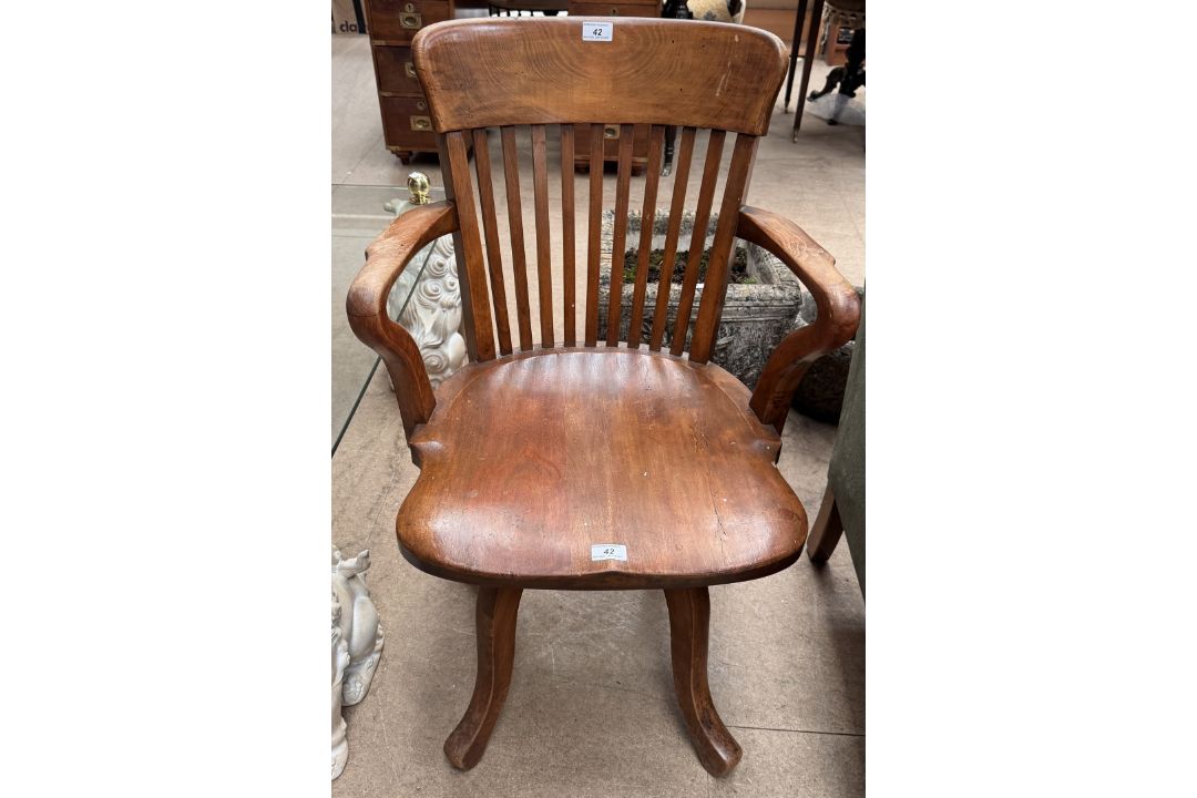 An elbow chair with a slat back and solid seat on four splayed legs