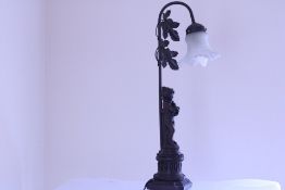 A figural table lamp with patinated metal column cast as a cherub beneath foliate detail, supporting