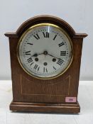 An oak cased mantle clock, six inch white enamel dial with roman numerals, three winding holes,