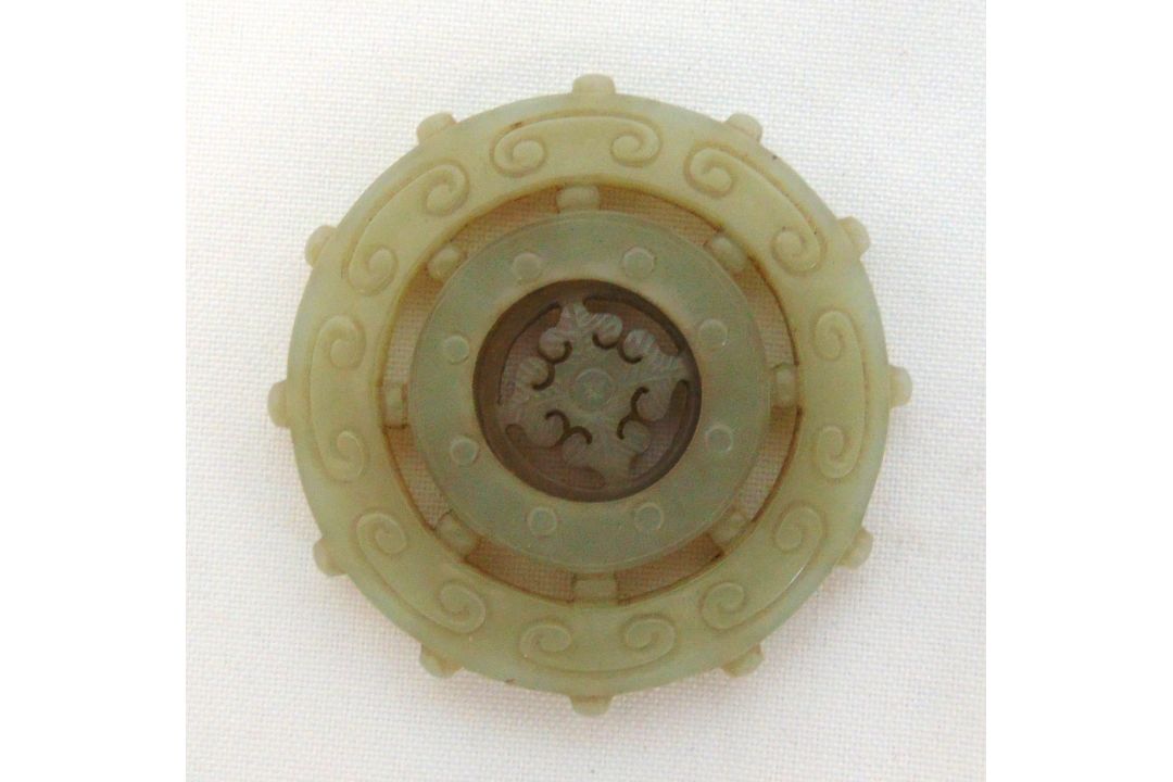 A Chinese Qing dynasty carved jade pendant of circular form engraved with geometric symbols, 6cm (